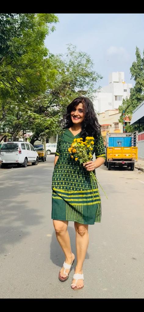 Girl wearing handblock printed green dress in Chennai and walking on the road, holding flowers